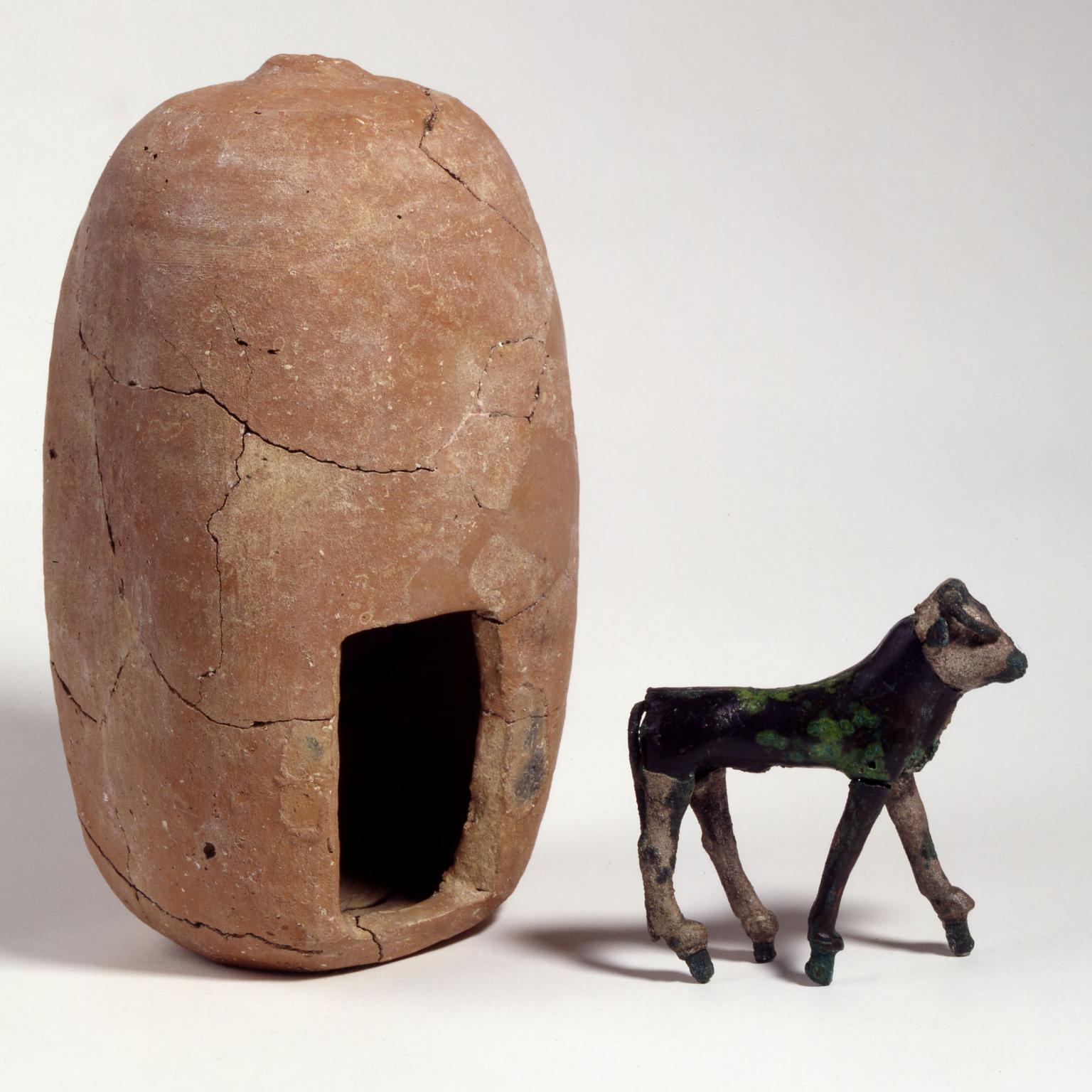 Silver calf figurine next to upright clay building with entrance.