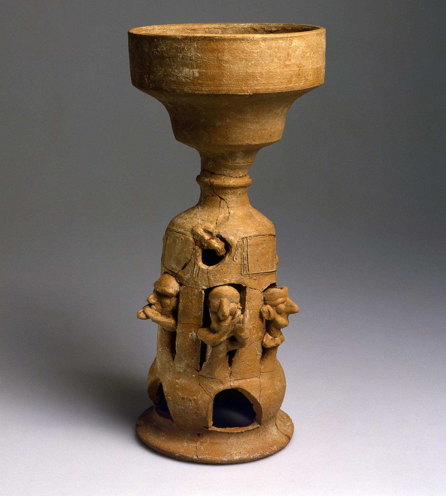 Ceramic stand decorated with carvings of musicians playing instruments.