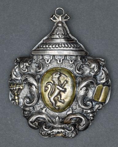 Silver amulet with designs around edge and lion in center.
