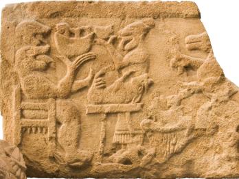 Stone relief of human-like monster in a chair and several animals and figures.