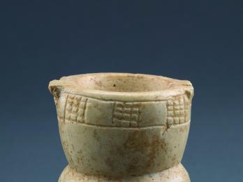 Limestone, goblet-shaped container with a footed base, a midsection with festoon pattern, and a deep bowl with checkerboard pattern on rim.