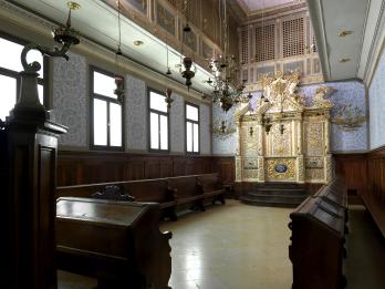 Photograph of room with pews along walls and gold Torah ark in center of back wall. 