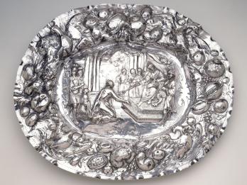 Metal tray with repoussé images of birds and fruit around rim, and image of king and subjects in center. 