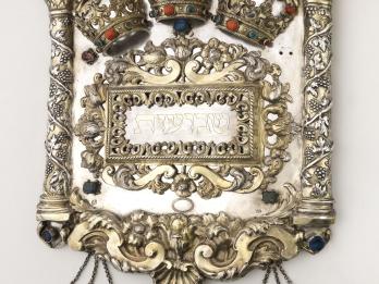 Torah shield decorated with vine-wrapped columns on either side, crowns across the top, and three smaller shields hanging from bottom. 