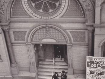 Photograph of building entrance with rose-shaped window and Hebrew inscription seen from above.