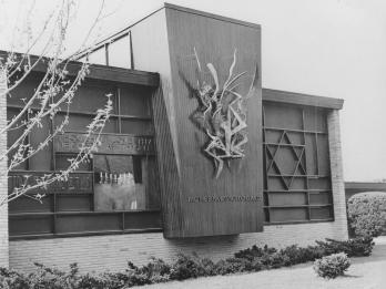 Exterior wall of synagogue featuring Star of David on the right side of the wall and a ribbon-like sculpture in the middle of the wall on a prominent vertical section that juts out from the rest of the wall, with inscription in English reading "And the bush was not consumed."