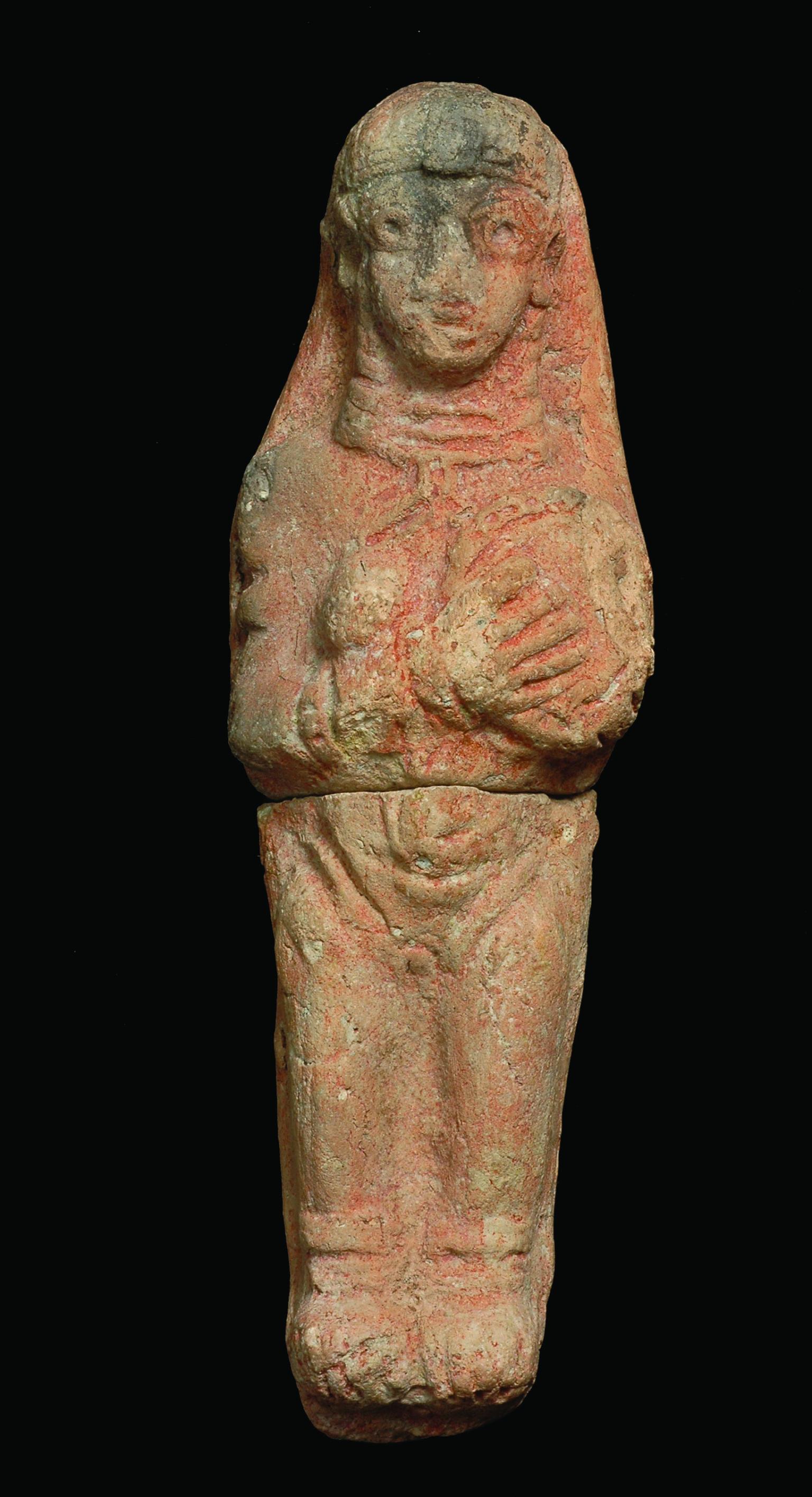 Terra-cotta figurine of woman wearing accessories holding a disk over left breast while right breast is exposed. 
