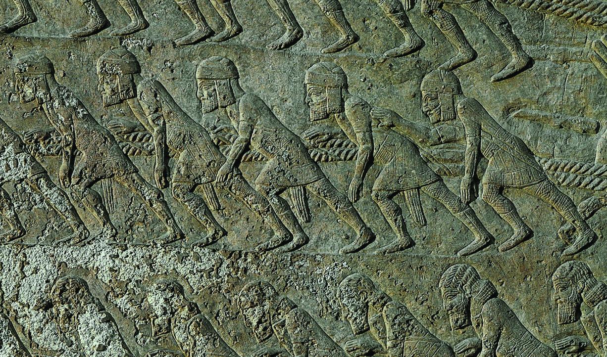 Wall relief showing workers wearing tunics, caps, and sashes, harnessed by shoulder straps to ropes and leaning forward. 