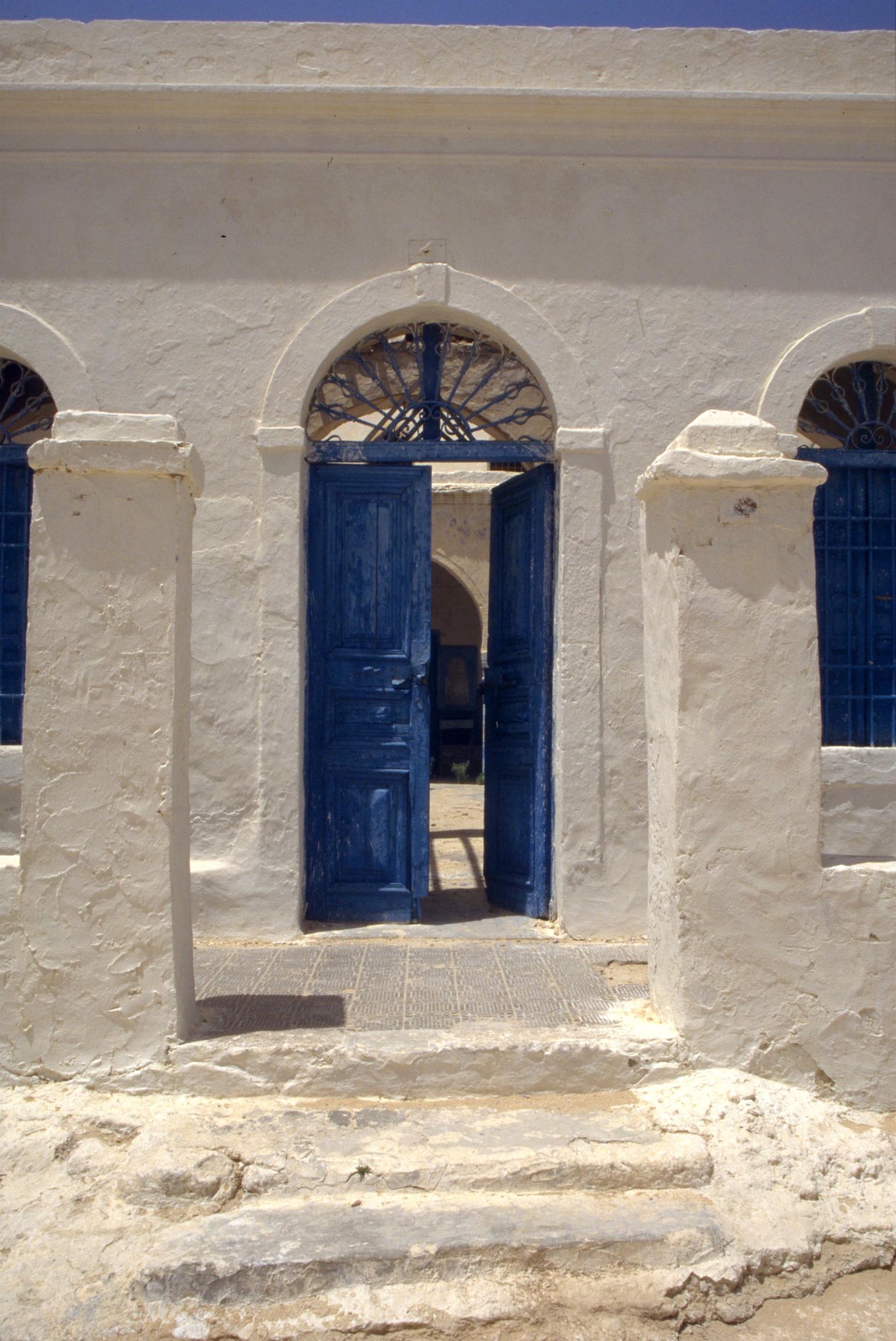 Building exterior with stone columns on either side of an open, arched doorway. 