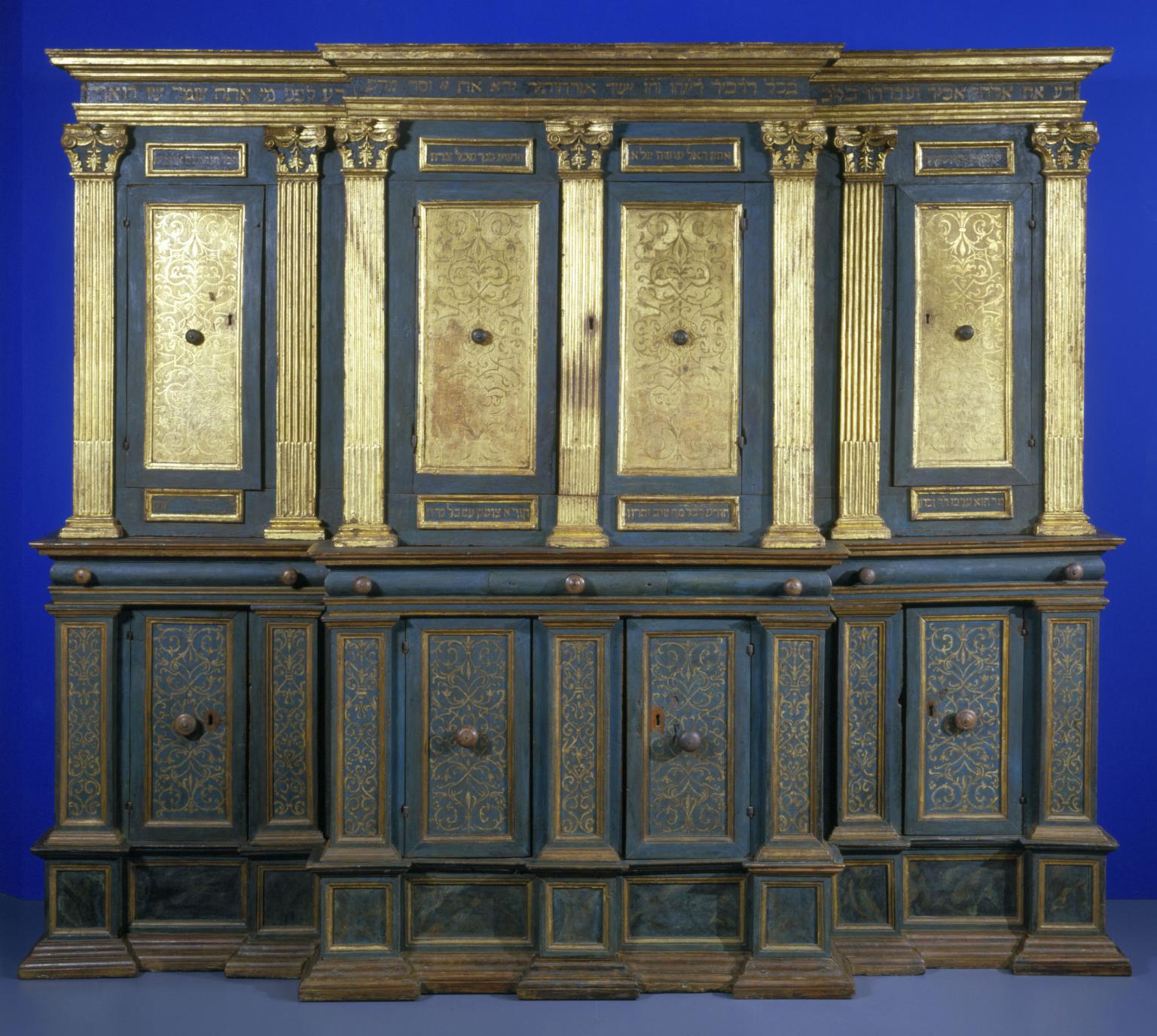Photograph of ornamental Torah ark chamber with gilded columns and doors with filigree and Hebrew writing. 