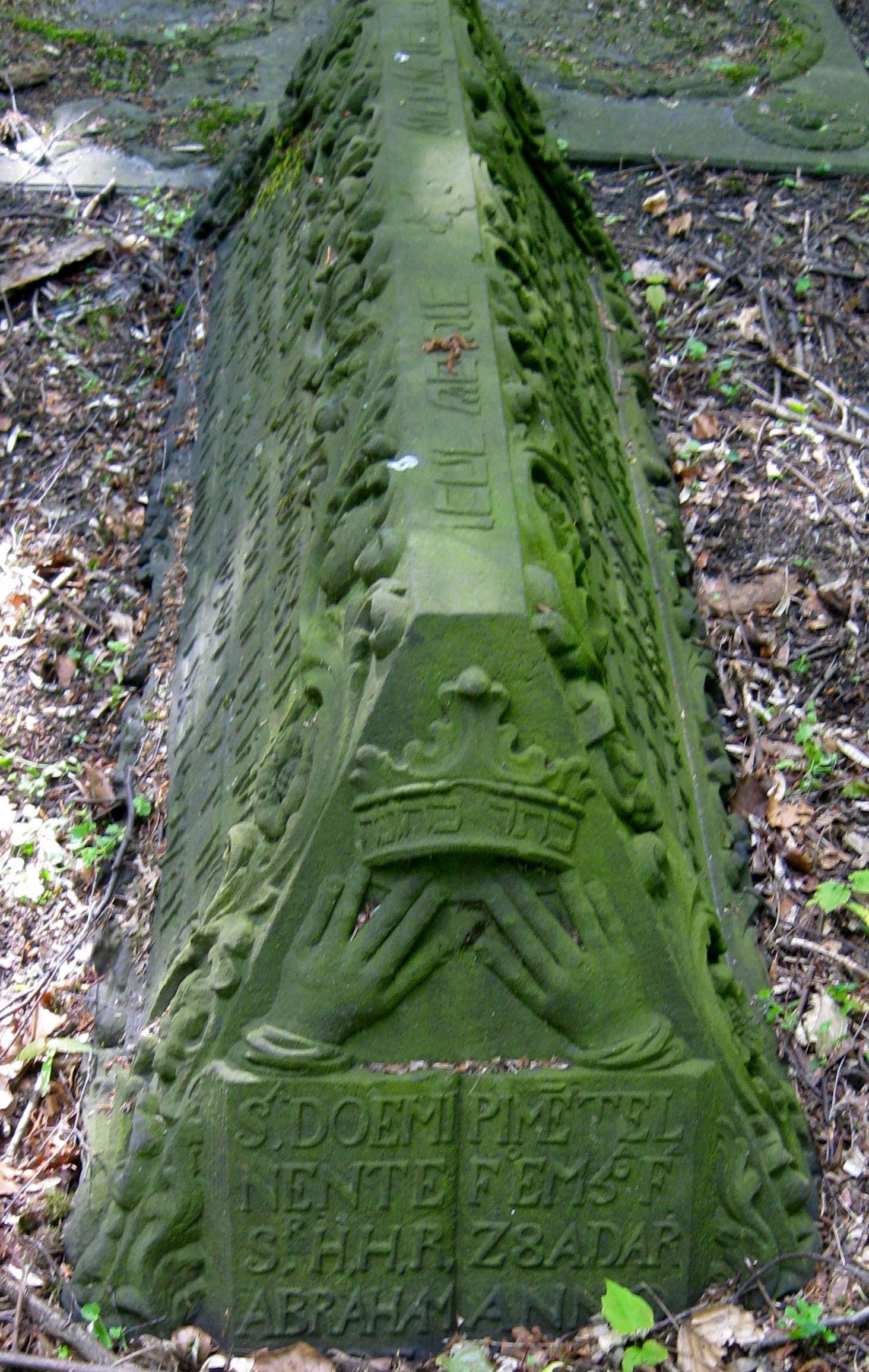 Tombstone in the shape of a triangular prism with carving of open book on short end with Hebrew and Portuguese inscriptions and decoration along length of stone. 