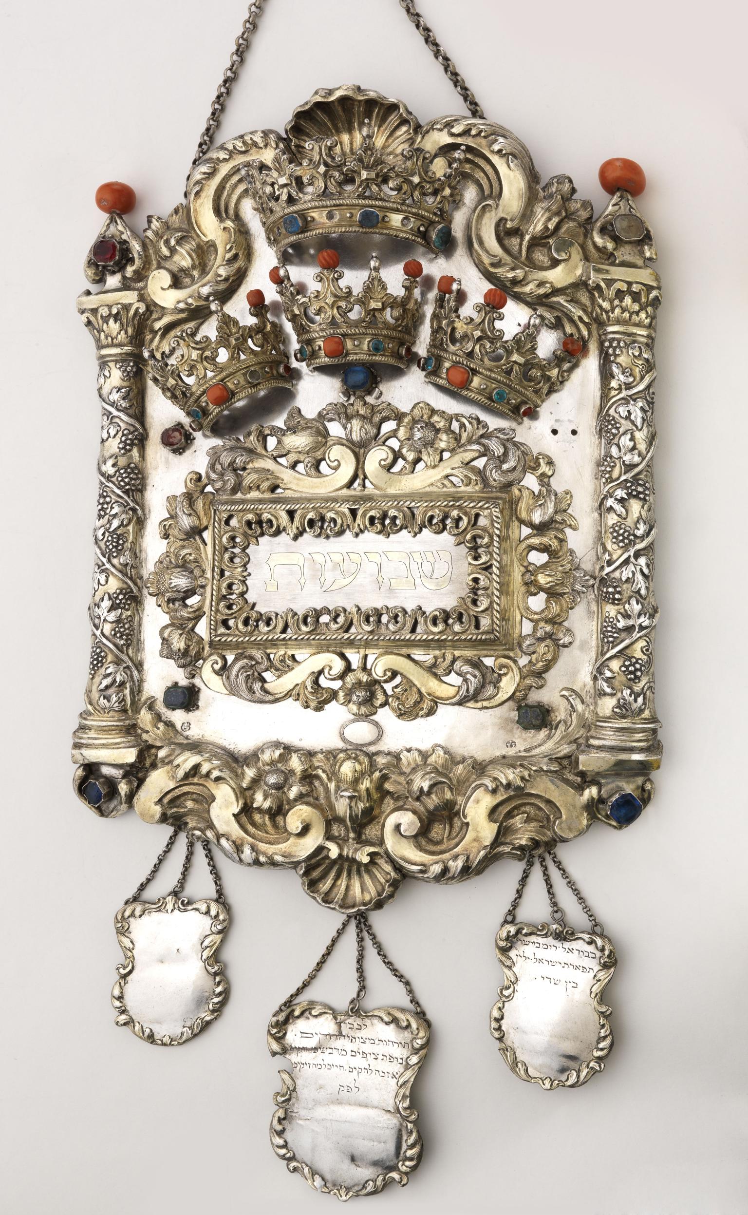 Torah shield decorated with vine-wrapped columns on either side, crowns across the top, and three smaller shields hanging from bottom. 