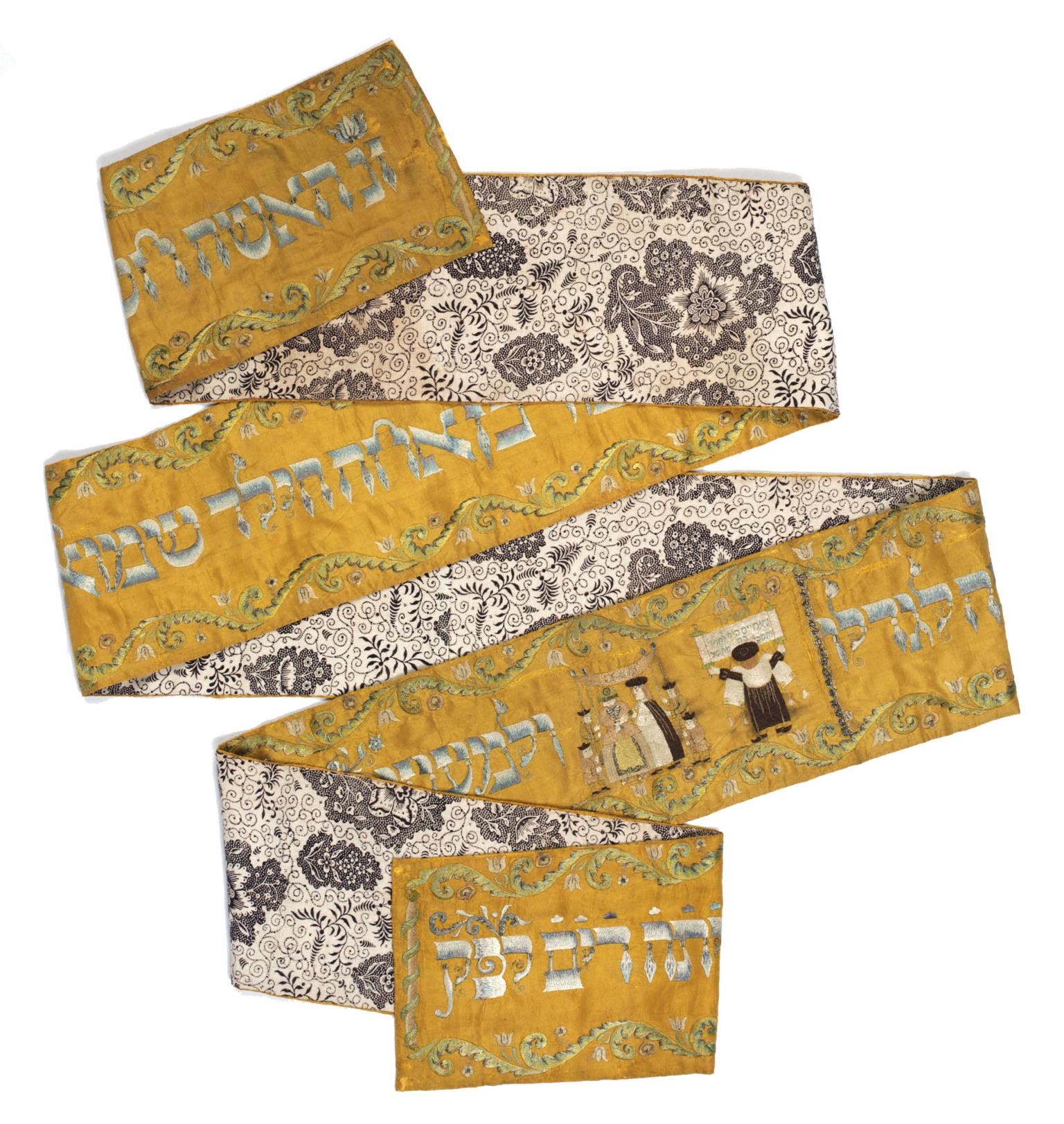Long rectangular cloth folded in several places, with floral design on one side and Hebrew text on the other side, with image of person reading from the Torah and couple under a wedding canopy. 