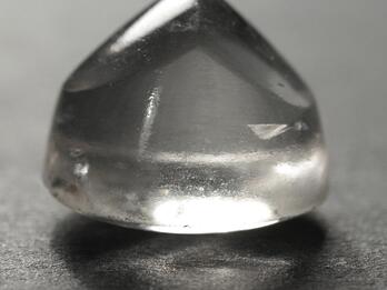 Photo of a transparent, slightly rough crystal piece with round bottom and crested top.