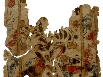 Fragment of a worn page depicting two birds facing each other among branches and fruits, with a decorated border.