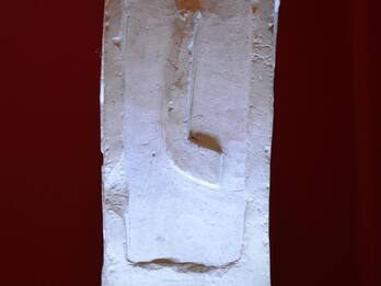 Photo of a weathered square stone slab inscribed with six lines of Latin.