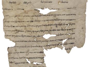 Damaged parchment with several large holes and tears and Hebrew script, largely in a paragraph with three lines of staggered words at the top, the first of which has floral decorations on each.