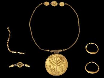 Photo of five pieces of gold jewelry, including a chain, a pair of earrings, and a necklace with a pendant featuring a candelabrum.