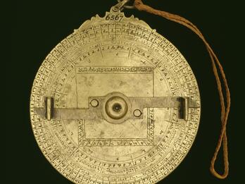 Circular, intricate brass object with Arabic and Hebrew inscriptions, geometric markings, and a rotating arm.