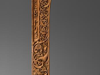Photo of a wooden architectural panel with a relief of intricate geometric and floral patterning and a line of Hebrew text down the left side.