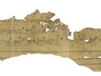 Irregular fragment of tattered manuscript with Hebrew lettering alternating between black, red, and gold, with vowels in black outline, and with small decorations disprersed among the words and smaller, vowelless lines of text below.