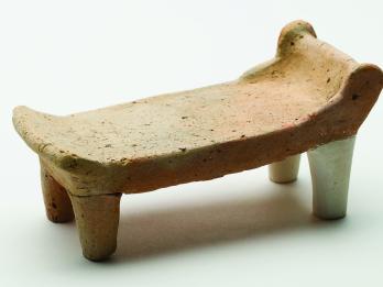 Terra-cotta bed with headrest and footrest standing on four legs.