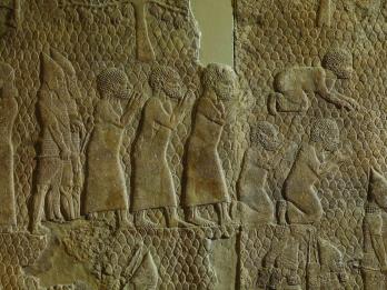Wall relief showing six men dressed in tunics, one prostrate and two kneeling, with two bearded soldiers behind them.