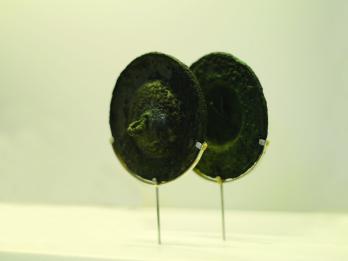 Pair of round bronze cymbals set on a modern wire display frame. 