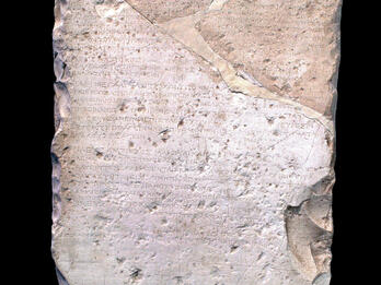 A weathered, roughly rectangular stone slab with ancient Greek inscriptions carved into its surface. Several parts are chipped, cracked, and uneven, with some repairs visible.