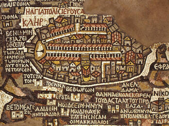 A detailed ancient mosaic map with Greek inscriptions, showing a walled city with buildings, streets, and landmarks, using earth-toned tiles. The map features intricate patterns and labeled areas throughout.