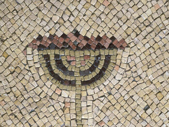 Ancient mosaic depicting a menorah with seven branches made from colored tiles, set against a beige background with geometric patterns.