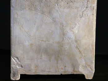 Side view of a stone ossuary featuring an inscription in Greek letters. The inscription is also transcribed below in clear handwriting.