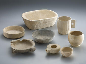 Six ancient ceramic jars and vessels of varying sizes and shapes, some with visible repairs, are arranged in two rows.