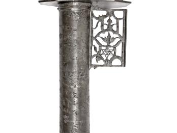 Metal cylindrical object with carving of lion holding axe on top, and decorative carving on bottom. 