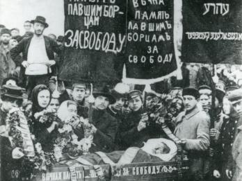 Photograph of crowd of people holding banners in Russian and Yiddish above a coffin.