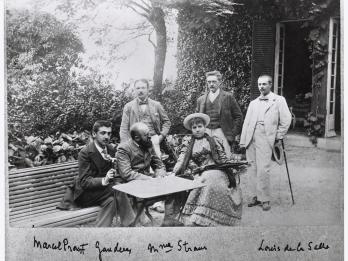 Photograph of several figures sitting at table in garden and signatures below as labels.