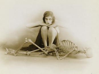 Photograph of female figure sitting behind skeleton.