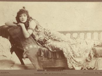Photograph of woman lying on chaise lounge facing viewer.