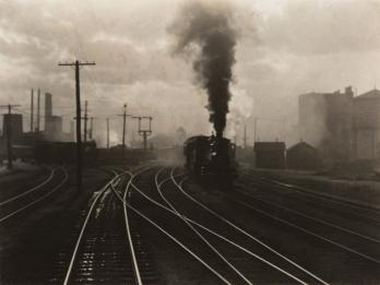 Photograph of train on tracks with large smoky cloud above it.