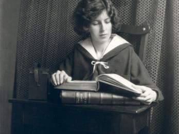 Photograph of figure seated at desk reading a book.