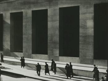 Photograph of silhouetted men walking next to high-columned building.