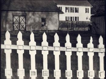 Photograph of fence in foreground and two houses in background.