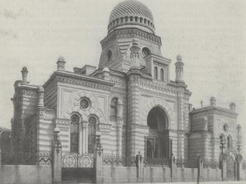 Street view of ornate building with archways, turrets, and domed roof, surrounded by fence.