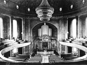 Photograph depicting organ and circular rows of benches, with large central chandelier.