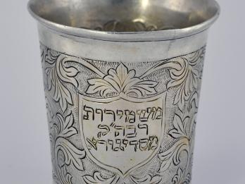 Silver cup etched with flowers, vines, and Hebrew letters in center.