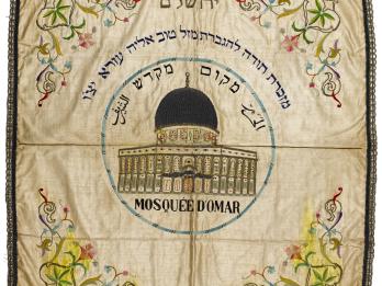 Embroided cloth with domed building in center, surrounded by Hebrew and Arabic text, and flowers in each corner.