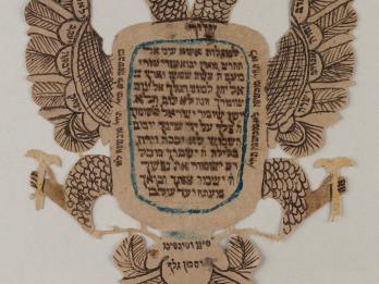 Paper cut in the shape of a two-headed eagle with spread wings, filled with Hebrew writing.