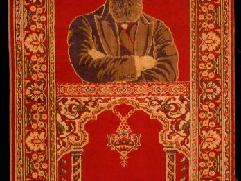 Rug depicting a bearded man with crossed arms on top half, and two columns and hanging lamp on bottom half, surrounded by decorative border.