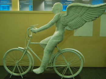 Sculpture of winged figure on bicycle.