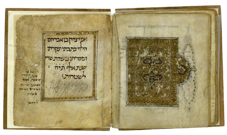 Book open to two facing pages, the right page with a gold, black, and blue geometric and floral design, and the left page with six lines of vowelless Hebrew text surrounded by a gold border, with a smaller note beside.